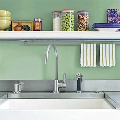 A green painted wall with a sink and shelf in front of it.