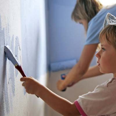 A child and parent painting a wall blue using a brush and roller.