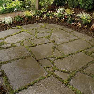 A patio with grass growing between stone that makes up the base.