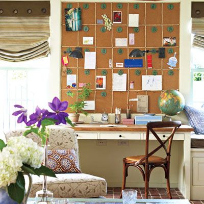 A wall covered in corkboard above a desk and chair. 