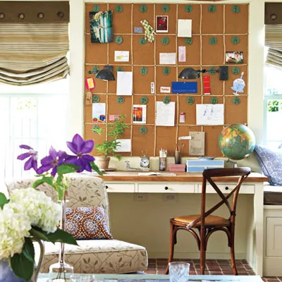 A wall covered in corkboard above a desk and chair. 