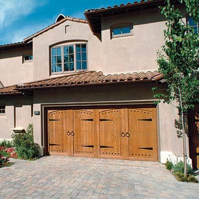 A Spanish-Colonial style house with mission style wooden garage door with black hardware.