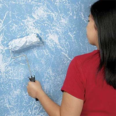 A woman using a paint roller to paint a wall blue.