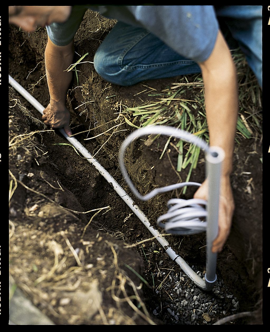 A man placing wiring in a trench for a lamppost.