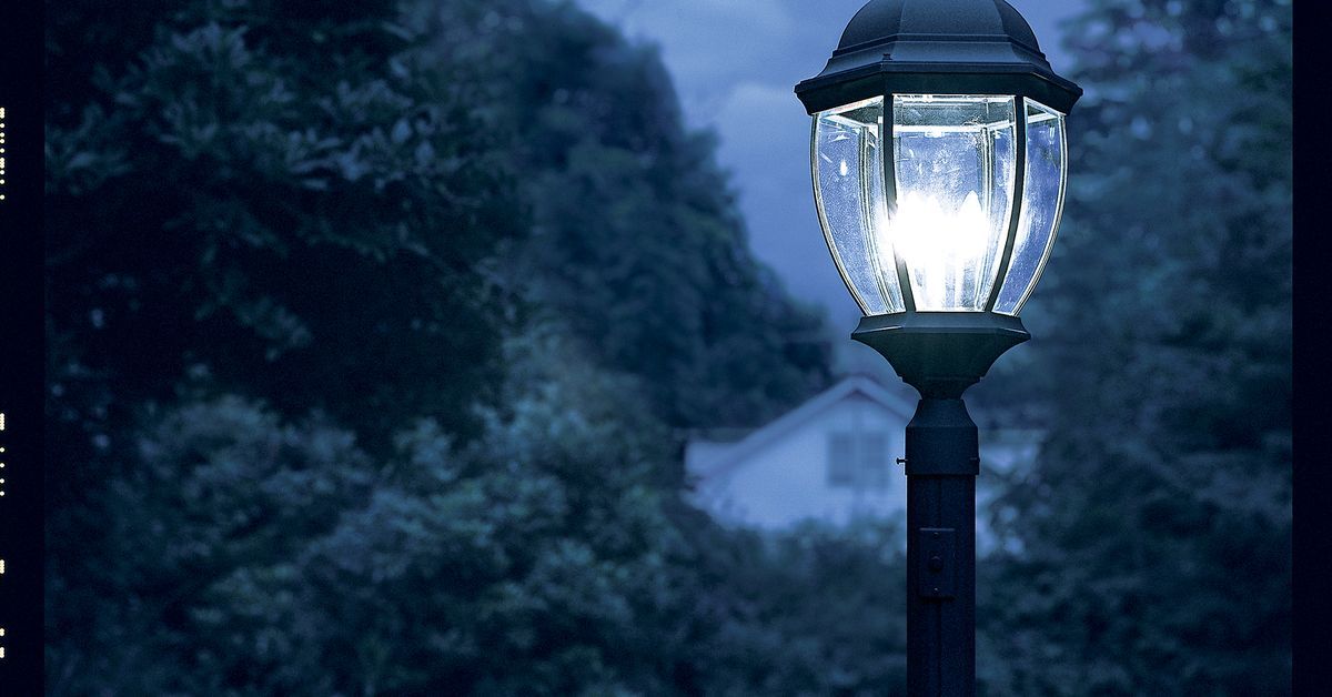 A lamppost installed in the grass shining on a dark night.