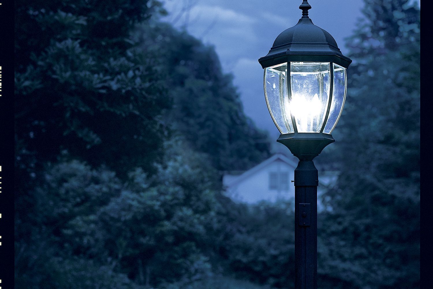 A lamppost installed in the grass shining on a dark night.