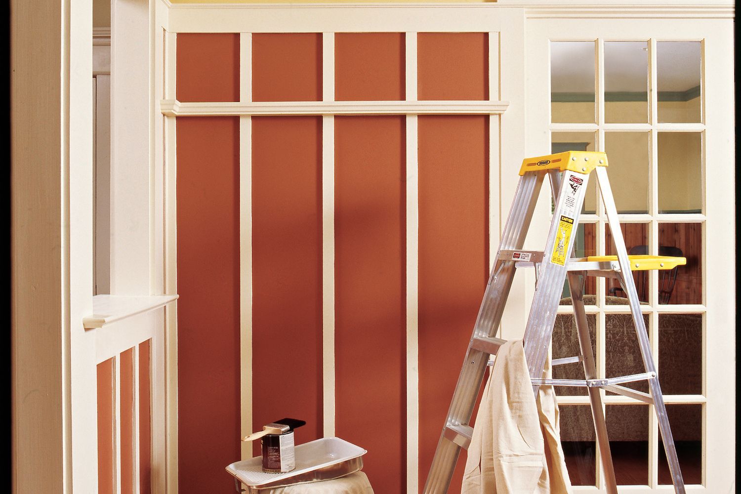A ladder and covered objects in a room being prepared for painting.