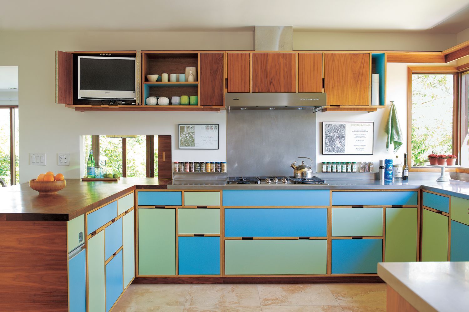 A modern kitchen features colorful laminate cabinets in blue and green, with wood accents.