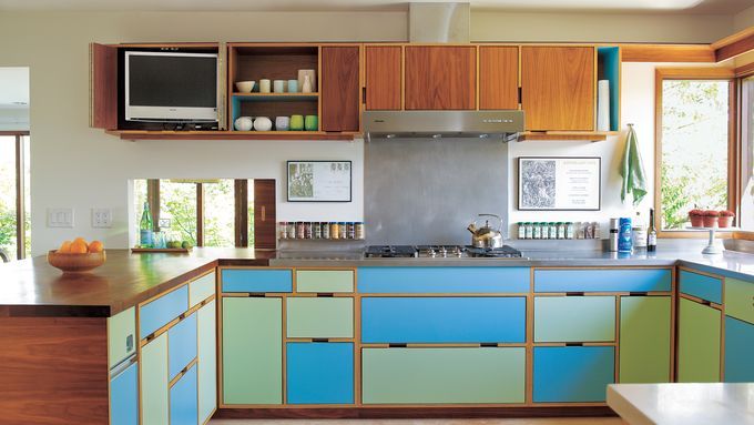 A modern kitchen features colorful laminate cabinets in blue and green, with wood accents.