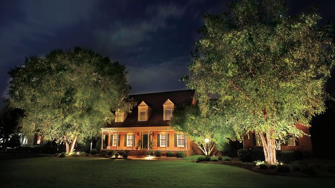 A landscape lighting system casting light on a tree and home at night.