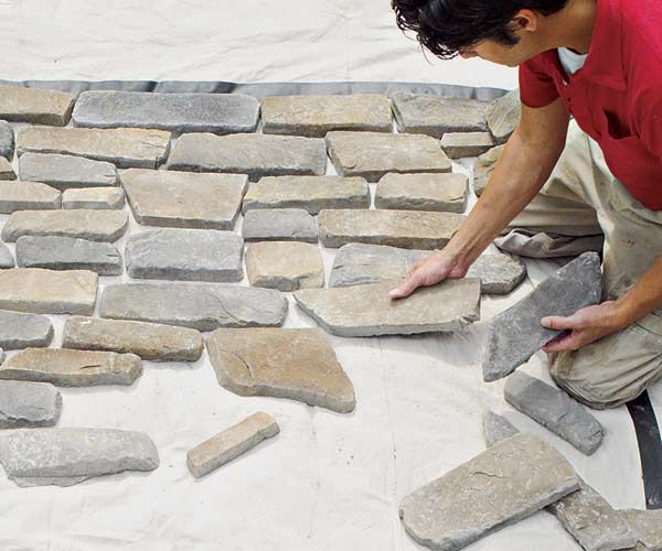 A man installs stones to become a stone veneer.