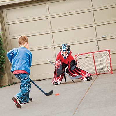 Two children playing hockey in front of a tan garage door.