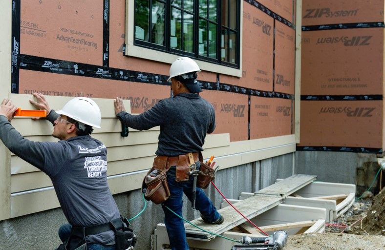 Contractors adding vinyl siding to a home.