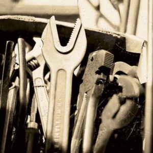 Antique wrenches sit in a box with other antique tools.