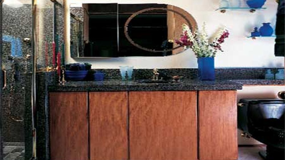 A bathroom with a black toilet and mirror over a black sinktop and brown cabinets