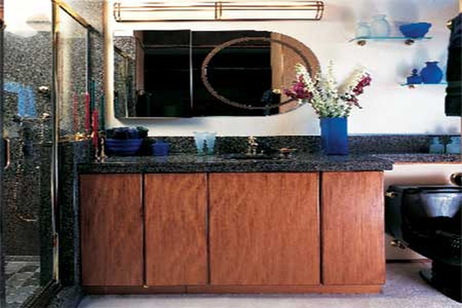 A bathroom with a black toilet and mirror over a black sinktop and brown cabinets