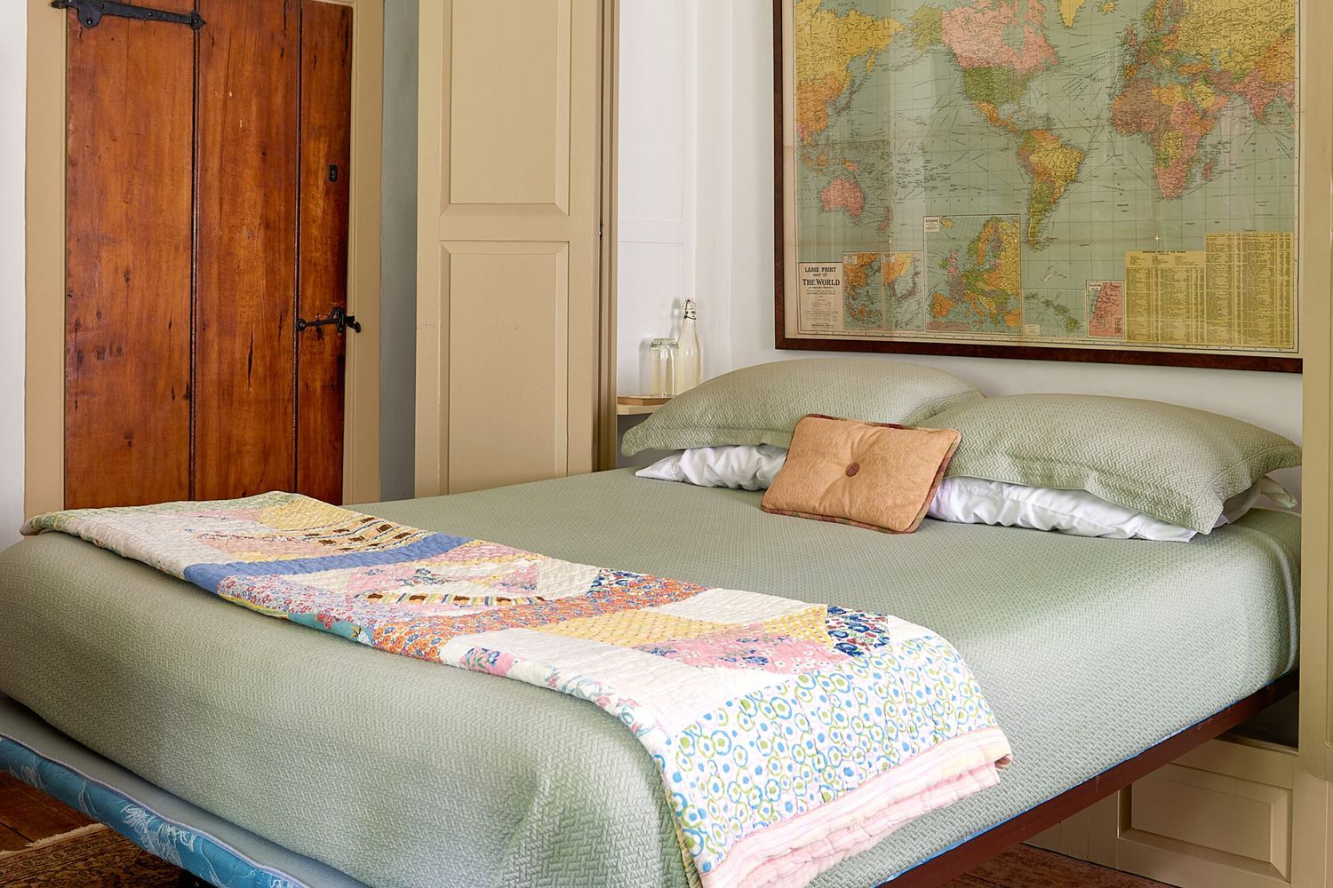 a murphy bed next to a door, it has a framed map above its head.
