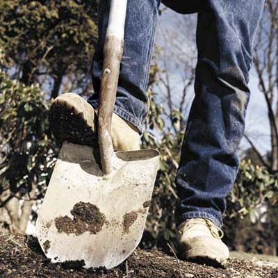 A person using their shoe to push a shovel into the ground.