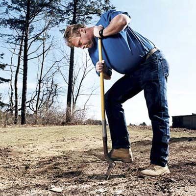 A man steps on a shovel as he digs it into the ground.