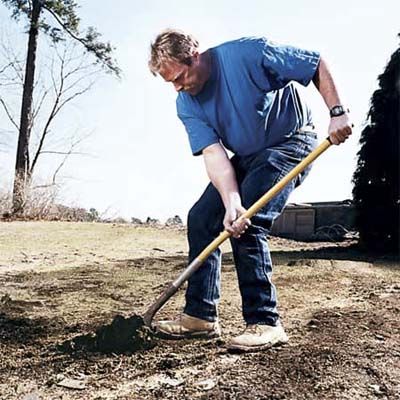 A man pries up dirt with his shovel as he digs.