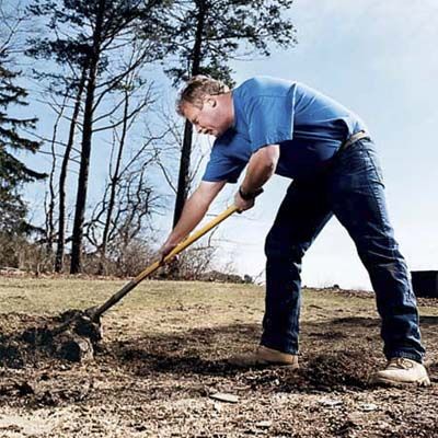 A man overextends his arms while lifting away dirt with his shovel.