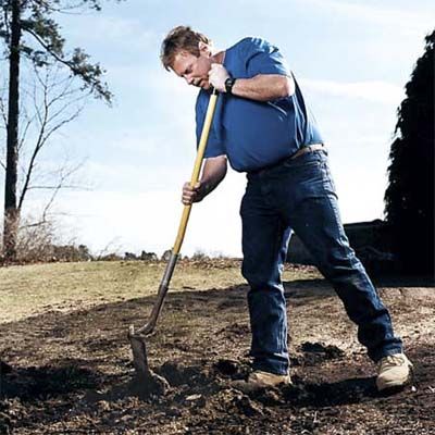 A man chops up dirt with his shovel before digging.