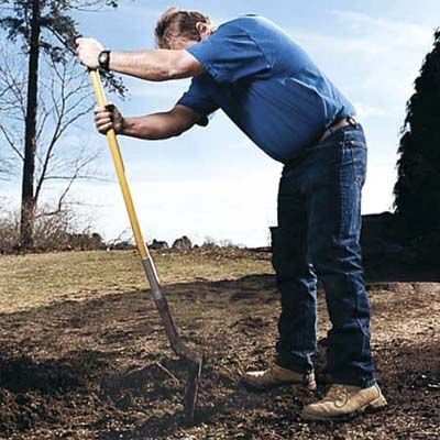 A man faces the shovel head the wrong way while chopping up dirt.