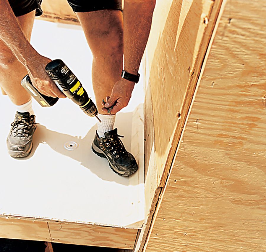 A man using a drill to apply a roofs underlayment.