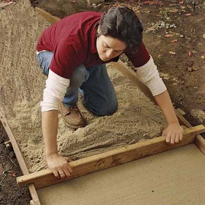 A person levels sand with a wood flooring scraps.