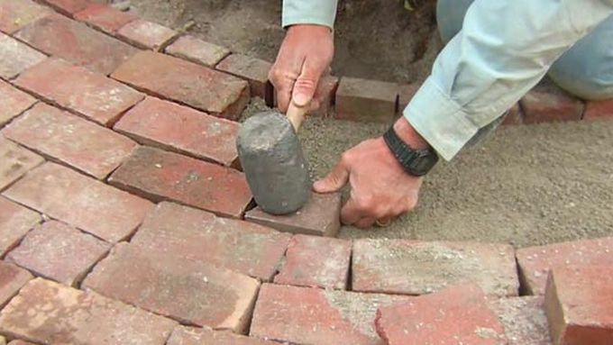 A man using a mallet to repair a brick walkway