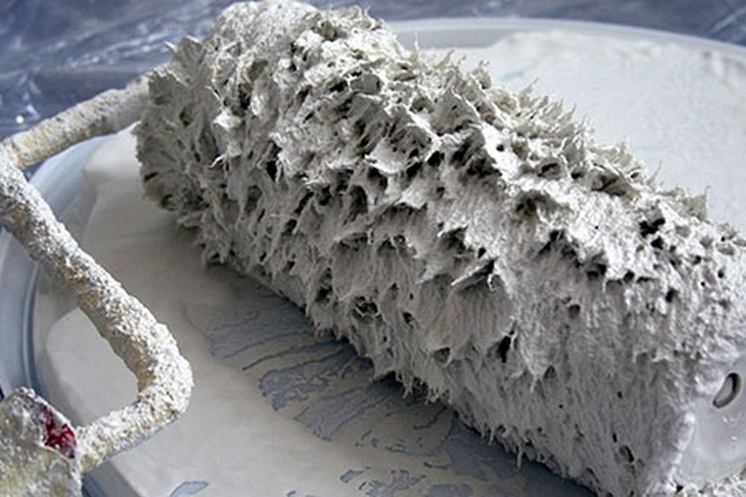 A paint roller being rolled in white paint.