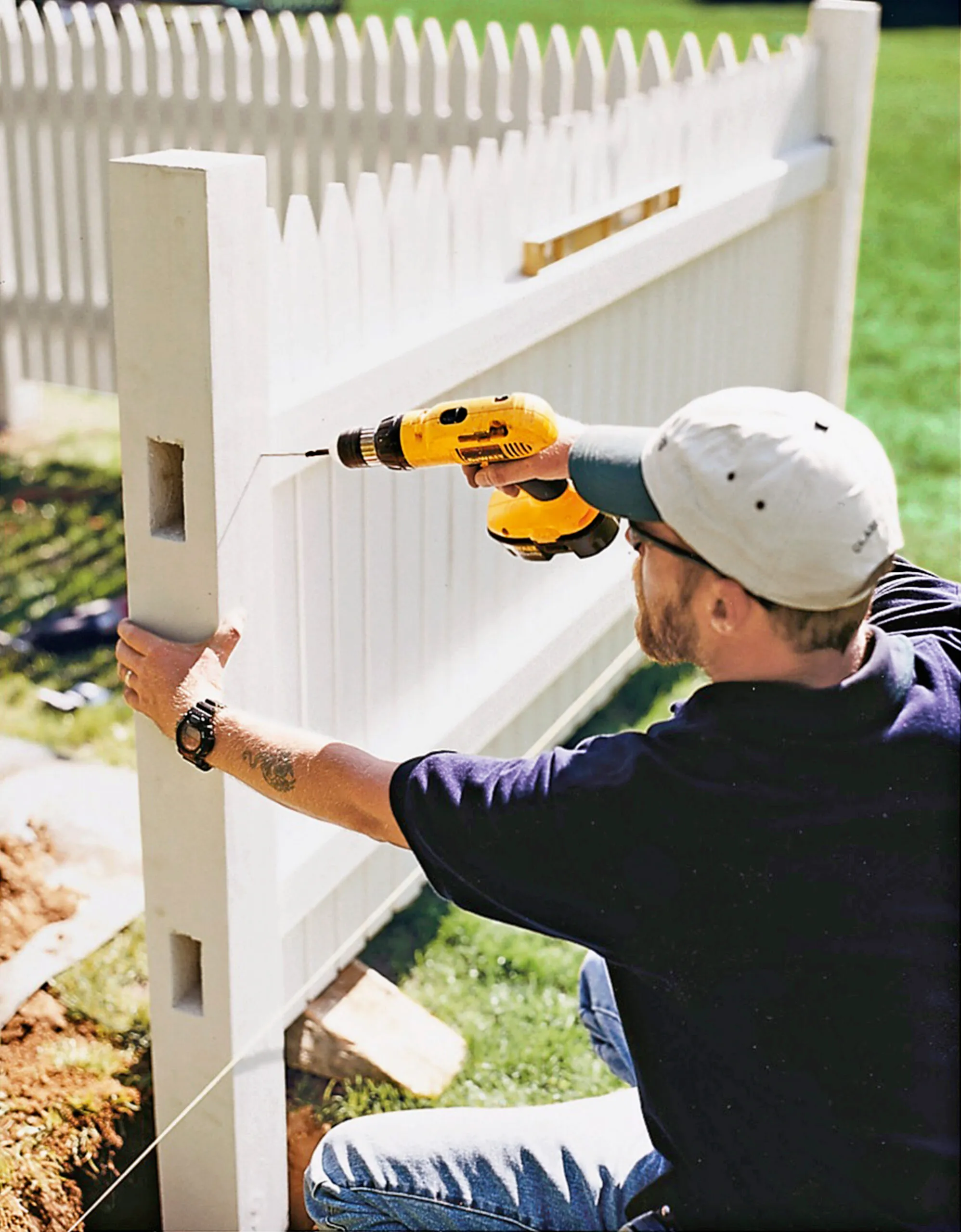 A man constructing a picket fence with a drill.