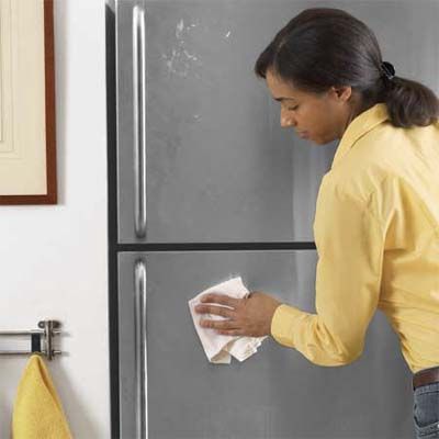 A woman wiping a fridge with a rag soaked in car wax.