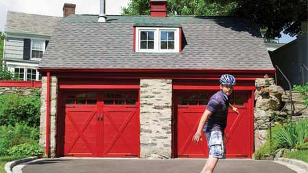 A person roller skating in front of a house with two red carriage-style garage doors.