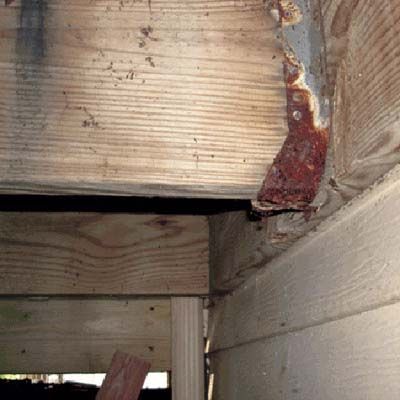 A rusted bracket holding up a piece of wood in a home.