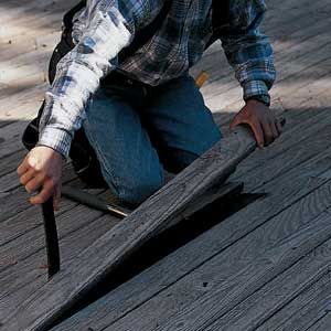 A man removes damaged boards from a deck to restore it.