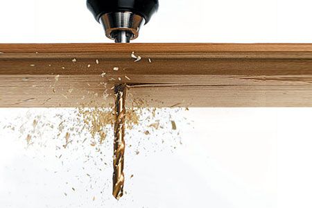 A drill bit pushing through a board of wood.