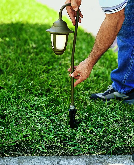 A man pushing a landscape light fixture into a lawn.