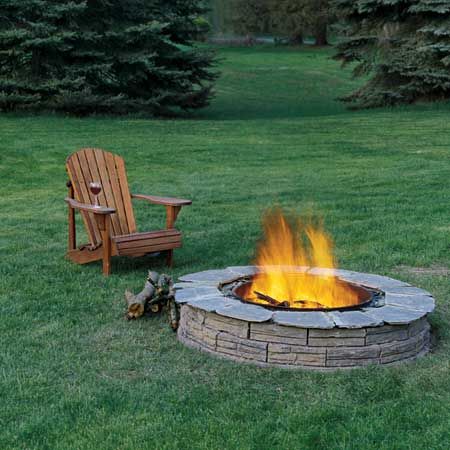 A stone fire pit beside a wooden chair with a glass of wine on its arm.