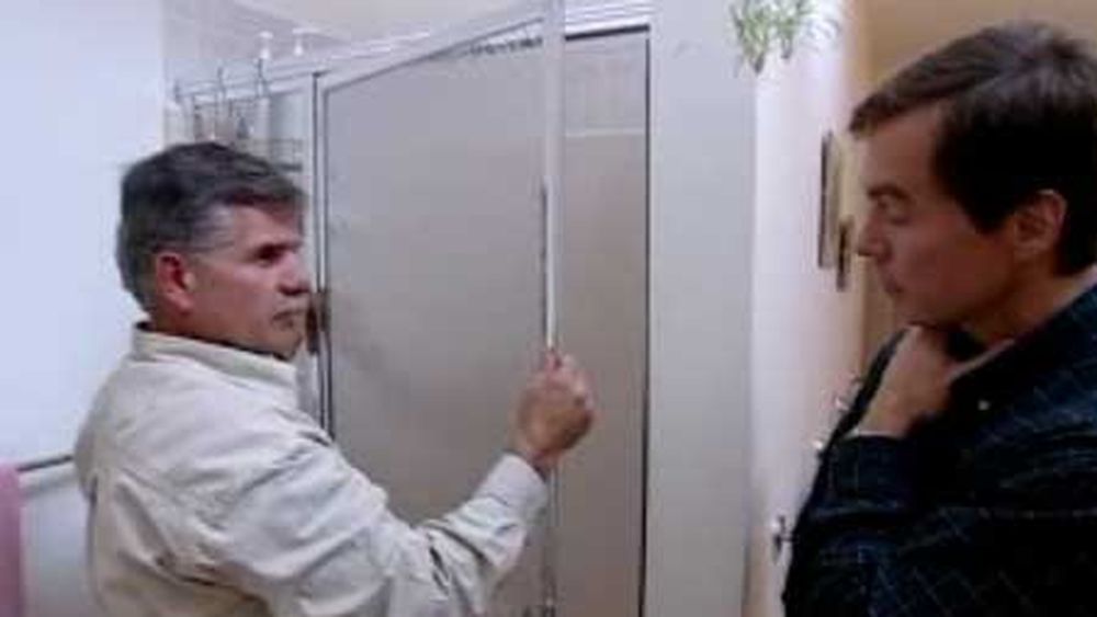 A man working on fixing a stuck shower door.