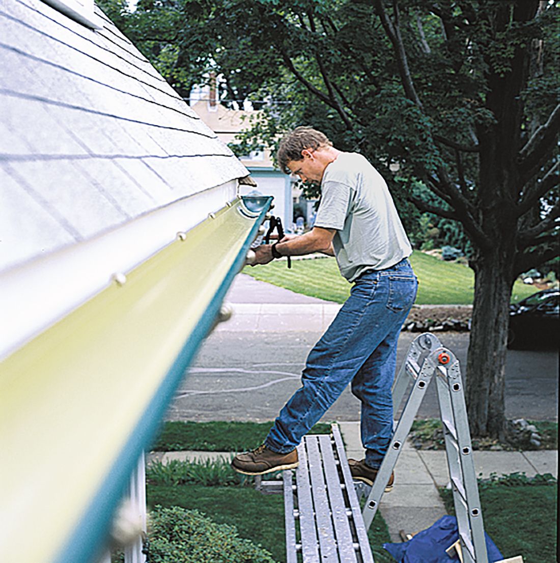 A man standing on a ladder to install a gutter on a home.