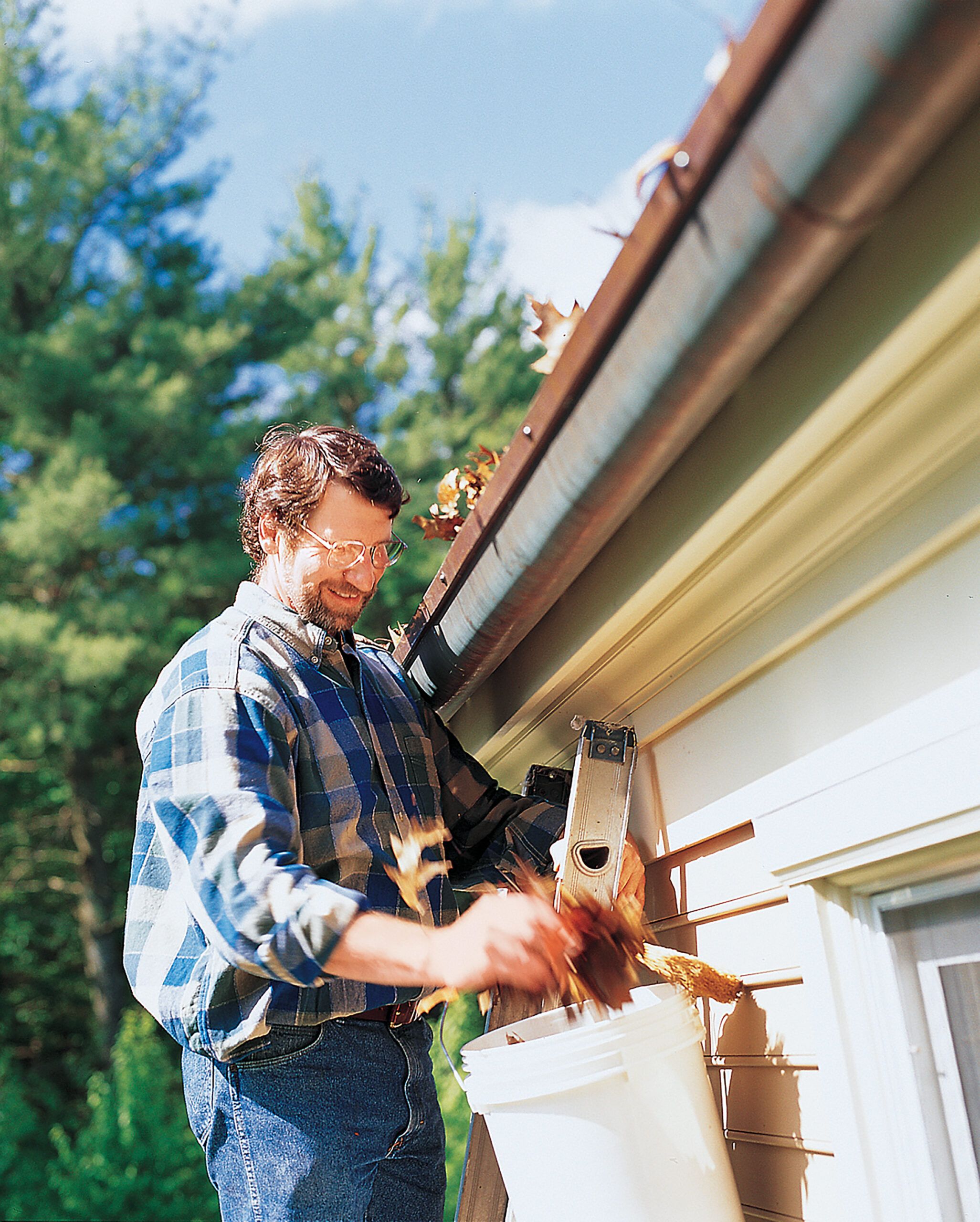 A man standing on a ladder and cleaning leaves out of a gutter