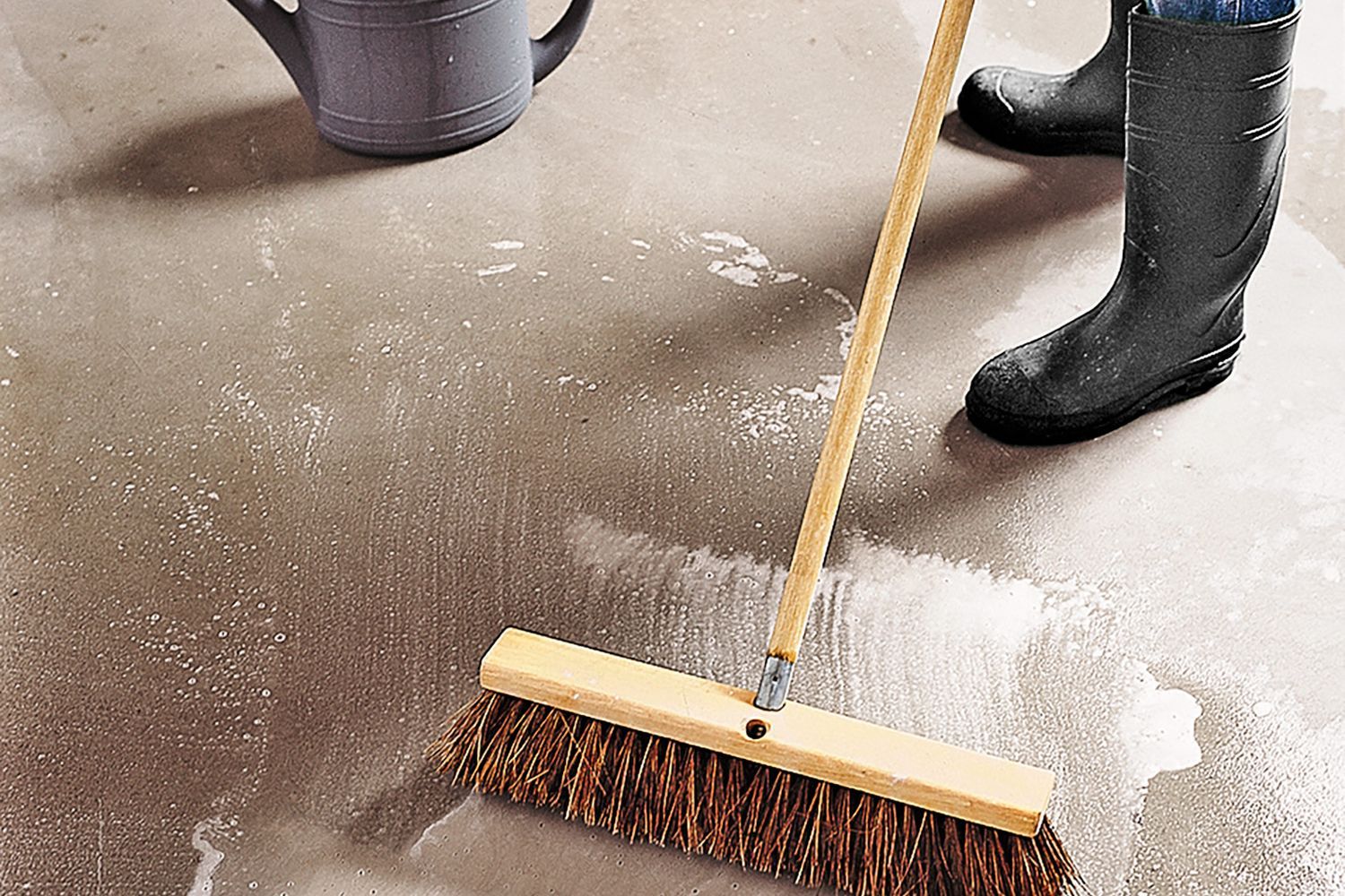 A man cleaning a garage floor with a push broom.