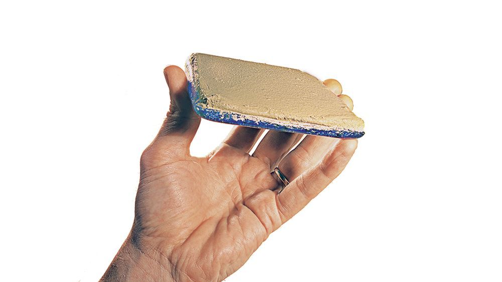 A hand holding a glass tile with adhesive attached to it for setting.