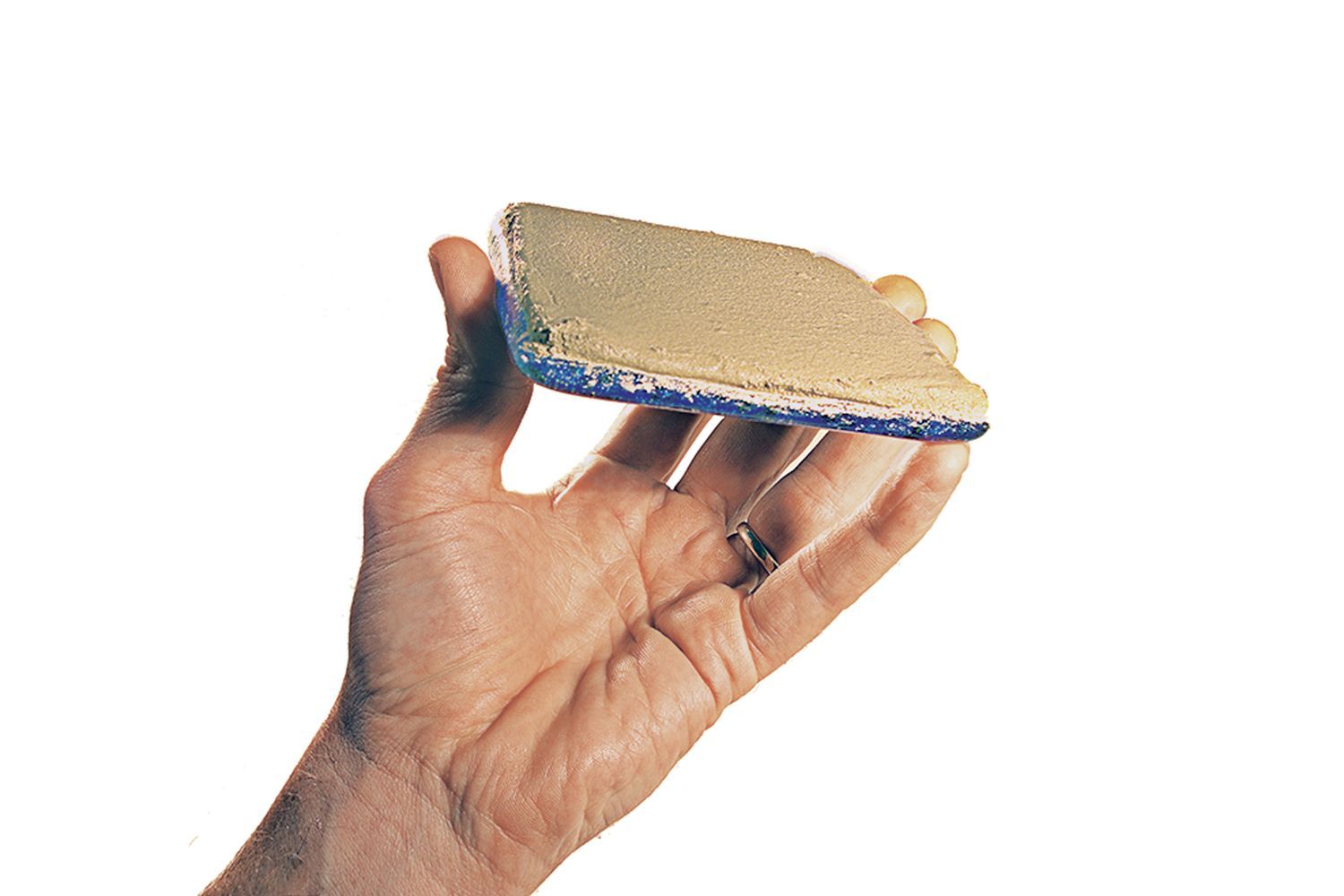A hand holding a glass tile with adhesive attached to it for setting.