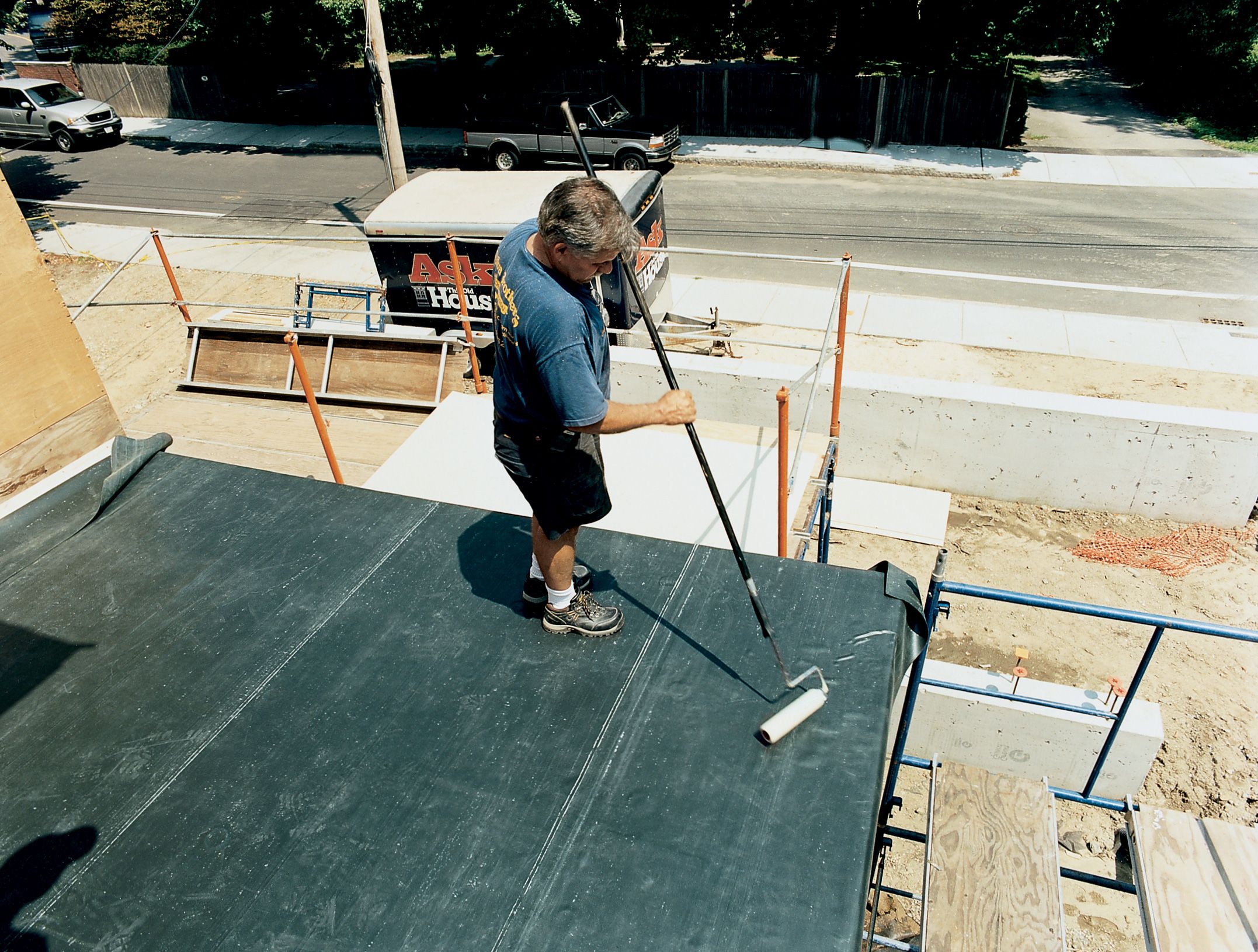 A man using a dry roller to adhere the waterproof membrane to a roof.