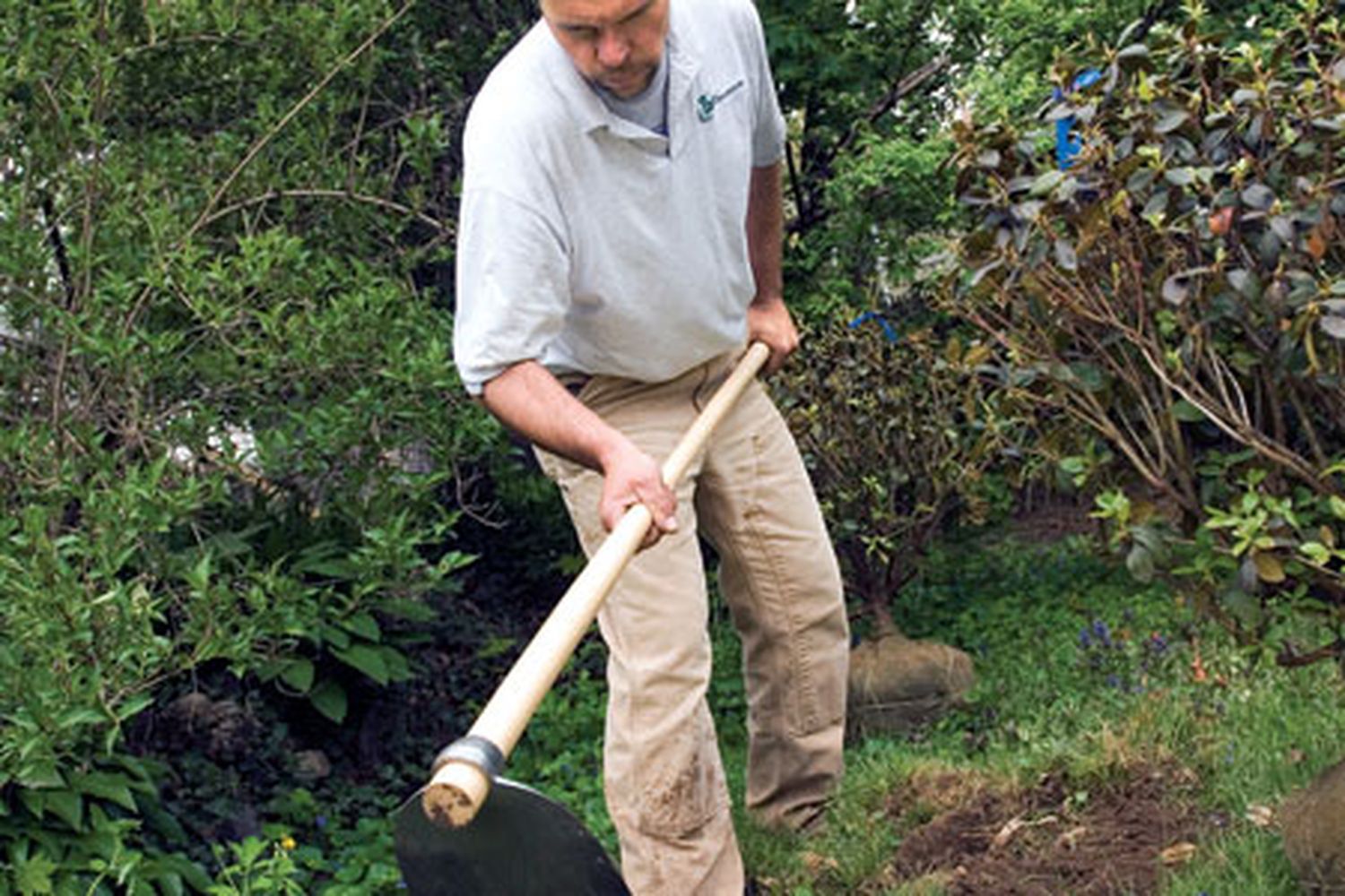 A man using a hoe to remove grass from a lawn.