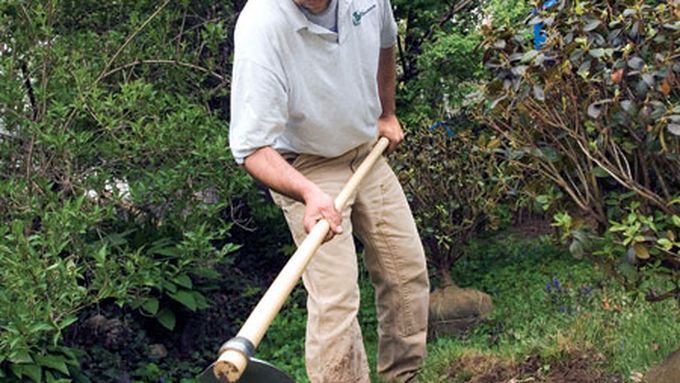 A man using a hoe to remove grass from a lawn.