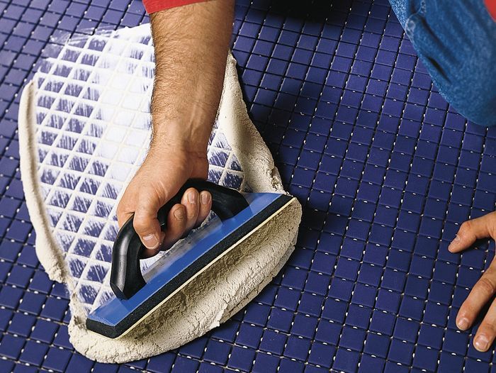 A man scrubbing tile grout with a cleaning fluid.