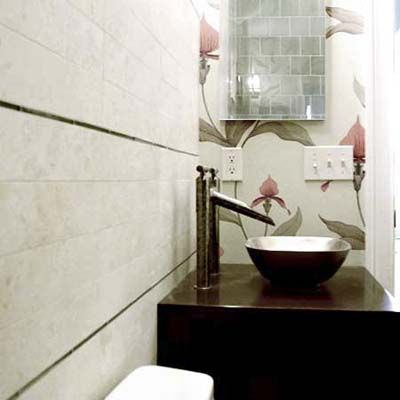 A half bath with a narrow layout features a dark wooden vanity, a vessel sink with a tall faucet, and a decorative floral-patterned accent wall with a mirror.